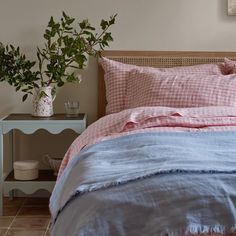 a bed with pink gingham comforter and pillows on it, next to a plant