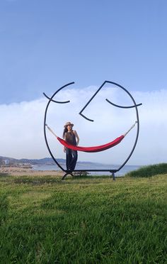 a woman sitting on top of a red hammock in the middle of a field