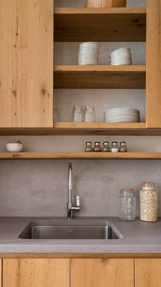 a kitchen with wooden cabinets and gray counter tops, white dishes on shelves above the sink