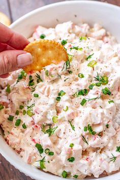 a hand dipping a cracker into a bowl of potato salad