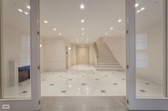 an empty white room with stairs leading up to the second floor and another hallway in the background