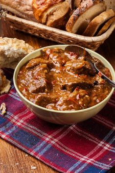 a bowl of stew next to bread on a table