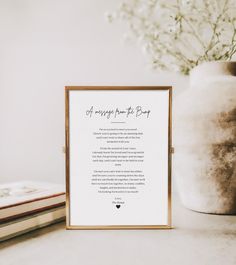 a framed poem sits next to a vase with flowers in it and a book on the table