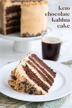 a slice of chocolate cake on a white plate with a cup of coffee in the background