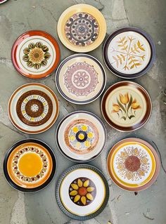 many different colored plates are arranged in a circle on the ground, with flowers painted on them