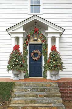 a blue front door decorated for christmas with wreaths and poinsettias on the steps