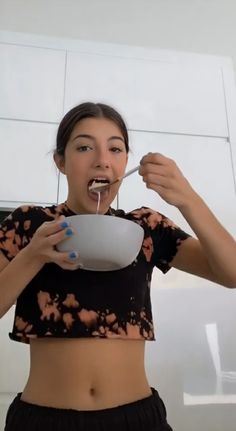 a woman is eating from a bowl and holding a spoon in her mouth with both hands