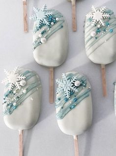 there are six pops decorated with frosting and snowflakes on them, one is white and the other is blue