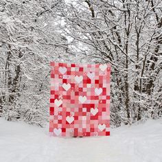 a red and white quilt sitting on top of a snow covered ground next to trees