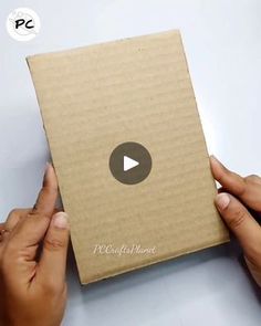 two hands holding an open box on top of a white table with a video playing in it