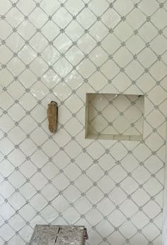 a white tiled wall with a small square window in the middle and a wooden box on the floor