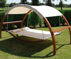 a wooden swing bed with a canopy over it in the middle of a grassy field