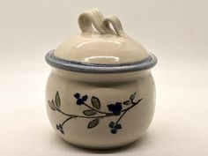 a white ceramic jar with blue flowers and leaves painted on the front, sitting on a white surface