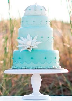 a three tiered blue cake sitting on top of a white table next to tall grass