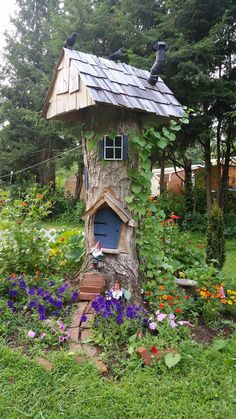 a tree stump with a house built into it in the middle of flowers and trees