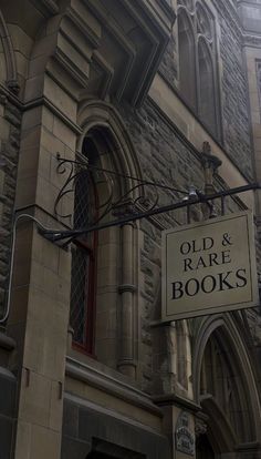 an old and rare book store sign hanging from the side of a stone building with arched windows