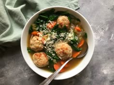 a white bowl filled with meatballs and vegetables next to a green napkin on top of a table