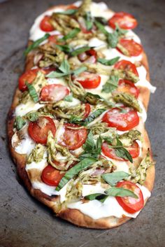 a pizza topped with tomatoes, cheese and green toppings