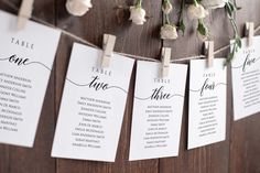 wedding seating cards hanging on a wooden wall with flowers in vases next to them