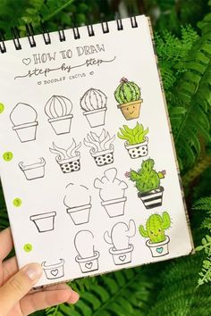 a hand holding up a notebook with drawings on it and green plants in the background