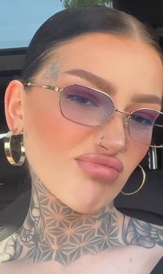 a woman with tattoos on her neck and glasses in the back seat of a car