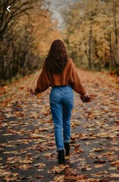 a woman walking down a leaf covered road