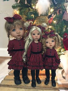 three dolls standing next to each other in front of a christmas tree