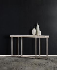 two white vases sitting on top of a wooden table next to a black wall