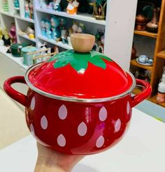 a hand holding a red pot with white polka dots and a strawberry on the top