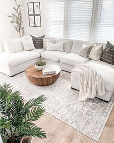 a living room with white couches and pillows on top of the rugs in front of two windows