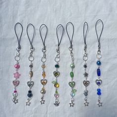 six different colored charms hanging from silver hooks on a white cloth covered tablecloth in various shapes and sizes