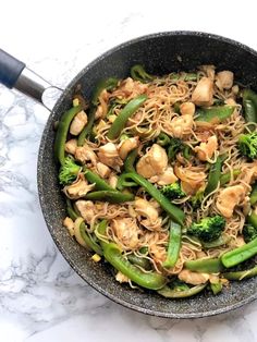 a wok filled with noodles and vegetables on top of a marble countertop next to a spatula