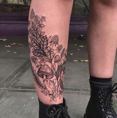 a woman's legs with flowers and leaves tattooed on her leg, while wearing black combat boots