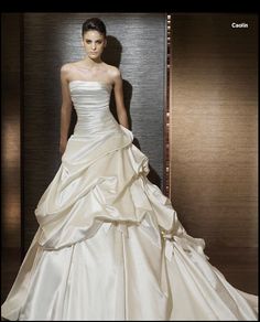 a woman in a white wedding dress standing next to a wall with her hand on her hip