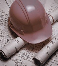 a hard hat sitting on top of blueprints next to rolled up construction plans