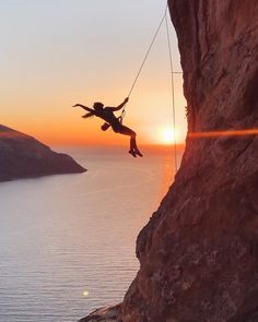 a person hanging from a rope above the ocean at sunset or sunrise, as seen from a cliff