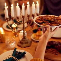 a person holding a plate with food on it at a table in front of candles