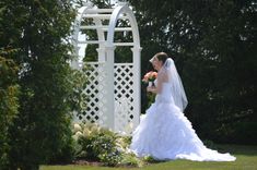 a woman in a wedding dress is standing near a gazebo and holding a bouquet