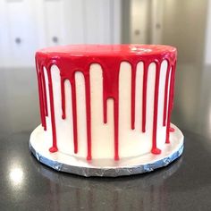 a red and white cake with dripping icing on it's side sitting on a table