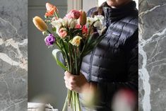 a woman holding a bouquet of flowers in front of a marbled window sill