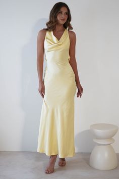 a woman in a yellow dress standing next to a white vase