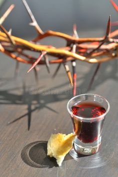 a shot of wine and a piece of bread on a table with crown of thorn branches in the background