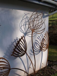 a white wall with metal art on it in front of a tree and grass area