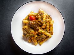 a white plate topped with pasta and meat covered in sauce on top of a black table