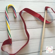 two candy canes on a white wooden table next to a red ribbon and stick