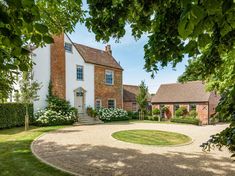 a large white house surrounded by lush green trees and bushes, with a circular driveway leading to the front door