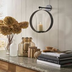 a table topped with books and vases next to a wall mounted candle holder filled with flowers