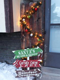 a wooden sign sitting in the snow next to a building with christmas lights on it