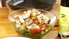 a salad in a bowl next to a bottle of wine on a wooden table with utensils