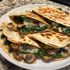 a white plate topped with three quesadillas covered in mushrooms and spinach